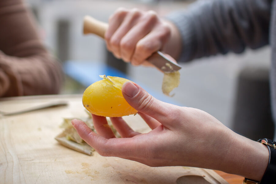 Dos manos pelando con un cuchillo pequeño una patata ya cocida con su piel