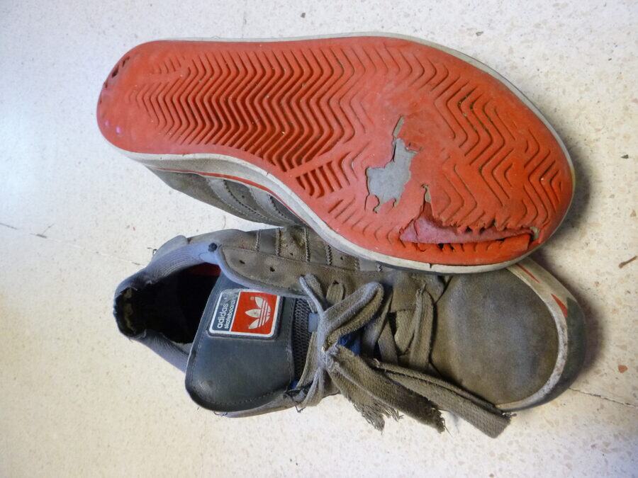 Par de zapatillas deportivas muy usadas, con la suela desgastada hasta agujerearse en la zona del antepié y el tejido deshilachado
